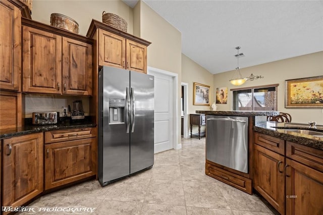 kitchen featuring pendant lighting, appliances with stainless steel finishes, vaulted ceiling, and dark stone countertops