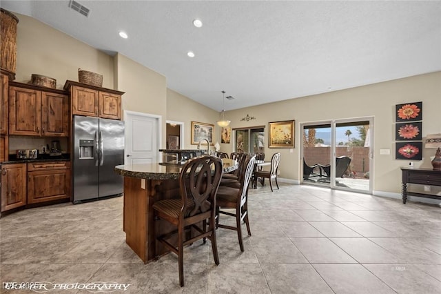 kitchen featuring a kitchen island, a breakfast bar, hanging light fixtures, light tile patterned floors, and stainless steel fridge with ice dispenser