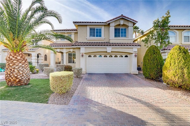 mediterranean / spanish home featuring decorative driveway, a tile roof, an attached garage, and stucco siding