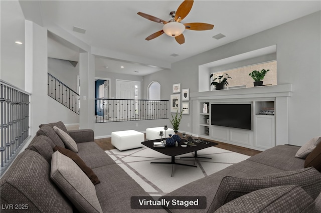 living area featuring ceiling fan, visible vents, baseboards, built in features, and stairway