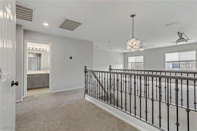 hall with carpet floors, visible vents, baseboards, and an inviting chandelier