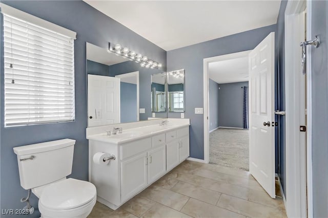 full bath with double vanity, toilet, a sink, tile patterned flooring, and baseboards