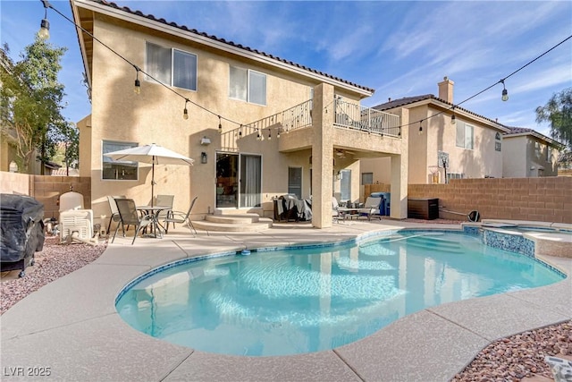 rear view of property with a patio, a balcony, fence, a pool with connected hot tub, and stucco siding