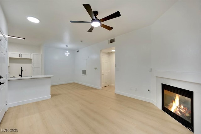 unfurnished living room featuring ceiling fan, sink, and light hardwood / wood-style floors