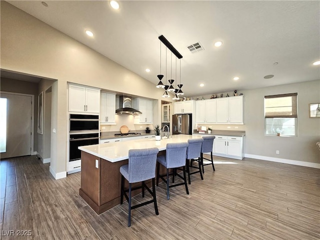 kitchen featuring decorative light fixtures, white cabinets, a large island, stainless steel appliances, and wall chimney exhaust hood