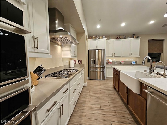 kitchen featuring white cabinetry, stainless steel appliances, sink, and wall chimney range hood