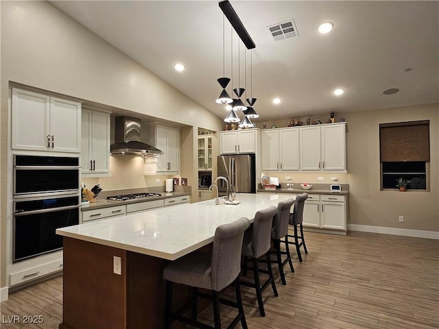 kitchen featuring appliances with stainless steel finishes, wall chimney exhaust hood, a large island, and decorative light fixtures