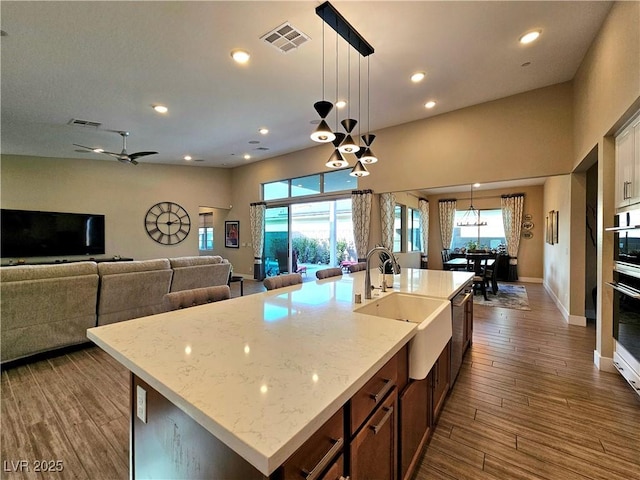 kitchen with dark wood-type flooring, sink, decorative light fixtures, an island with sink, and light stone countertops