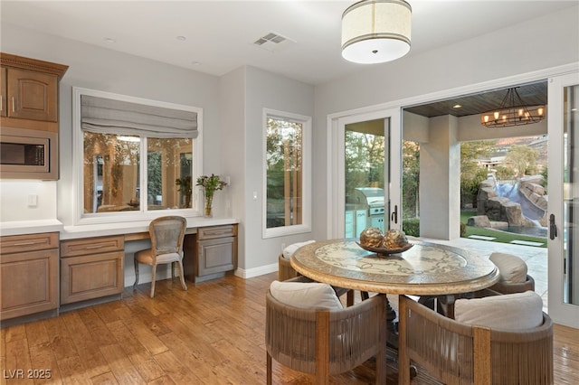 dining room with built in desk, light hardwood / wood-style floors, and a chandelier