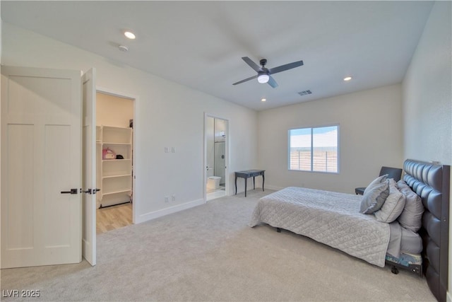 bedroom with a walk in closet, light colored carpet, connected bathroom, and ceiling fan