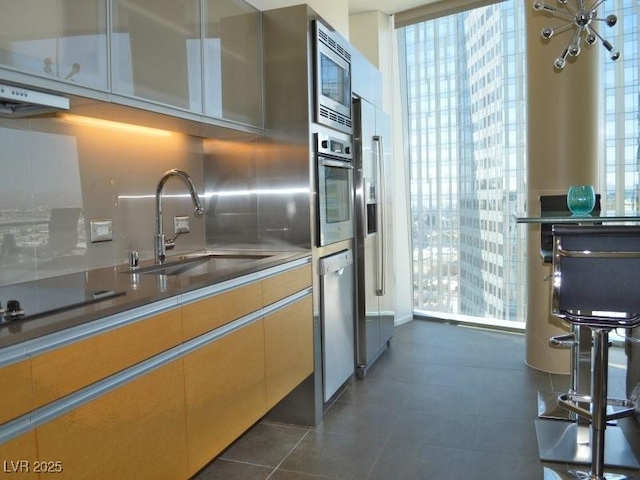 kitchen with sink, appliances with stainless steel finishes, backsplash, expansive windows, and dark tile patterned flooring