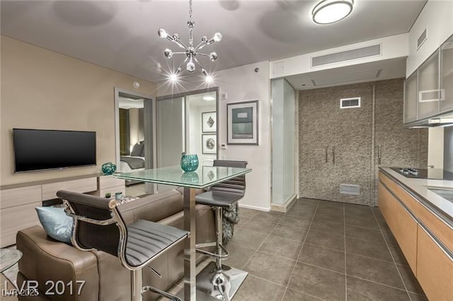 interior space with a kitchen breakfast bar, dark tile patterned floors, black electric stovetop, a notable chandelier, and light brown cabinets