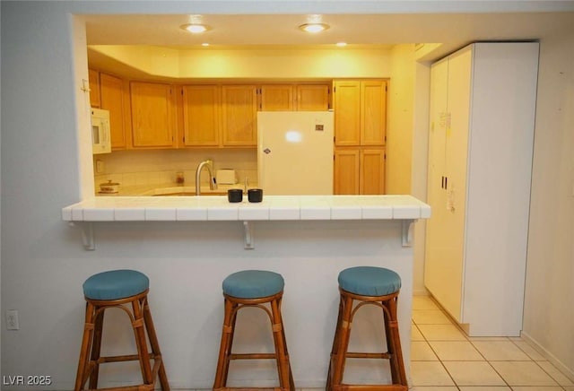 kitchen featuring white appliances, tile countertops, a breakfast bar area, and light tile patterned flooring