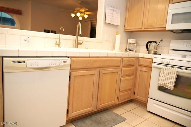 kitchen featuring light tile patterned floors, white appliances, sink, ceiling fan, and tile counters