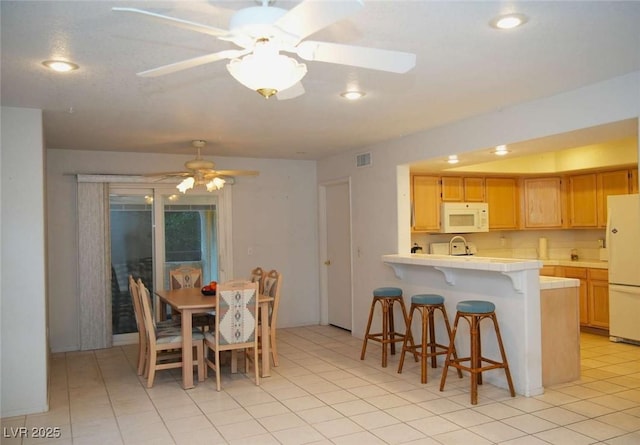 kitchen featuring white appliances, ceiling fan, a kitchen bar, light tile patterned flooring, and light brown cabinets