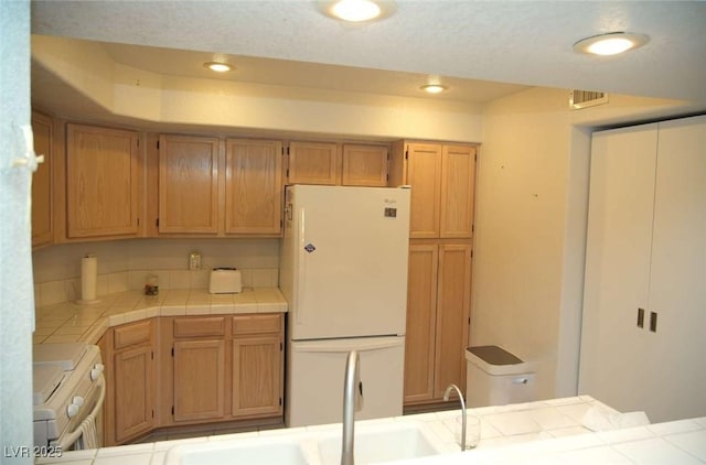 kitchen with white fridge, sink, tile countertops, and stove