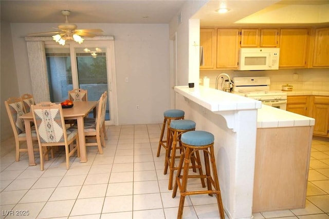 kitchen with white appliances, light tile patterned floors, a kitchen breakfast bar, kitchen peninsula, and ceiling fan