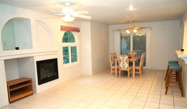 dining room with light tile patterned floors, a large fireplace, and ceiling fan