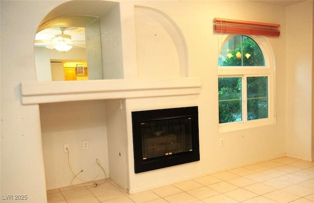 unfurnished living room featuring a glass covered fireplace, a ceiling fan, and tile patterned flooring