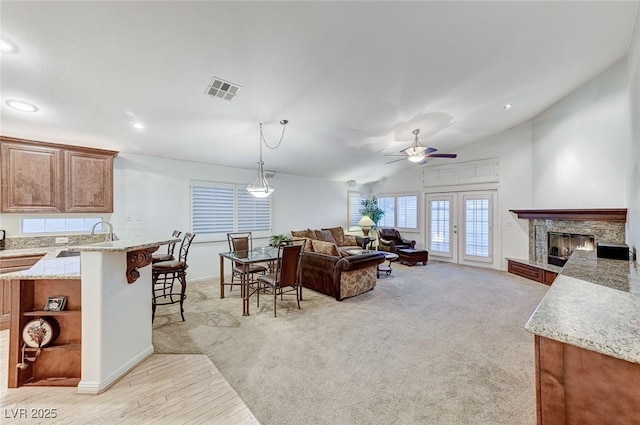 carpeted living room featuring french doors, a stone fireplace, sink, vaulted ceiling, and ceiling fan