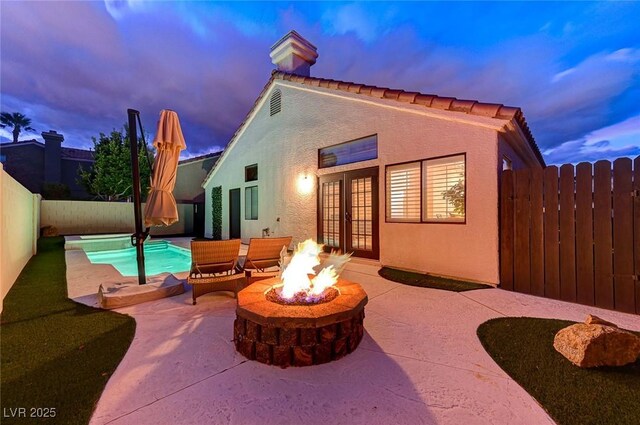 back house at dusk with a fenced in pool, a fire pit, a patio area, and french doors