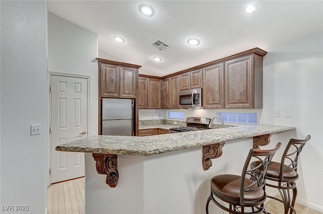 kitchen featuring a breakfast bar, stainless steel appliances, kitchen peninsula, and light stone countertops