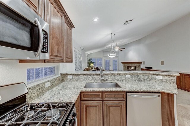 kitchen featuring sink, stainless steel appliances, light stone countertops, decorative light fixtures, and vaulted ceiling