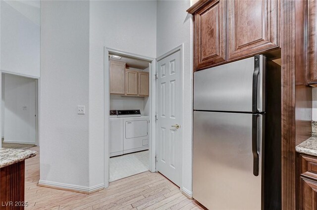 kitchen featuring independent washer and dryer, stainless steel fridge, light stone counters, and light hardwood / wood-style floors