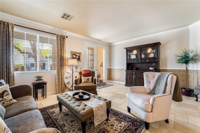 living area with a wainscoted wall, visible vents, crown molding, and stone tile floors