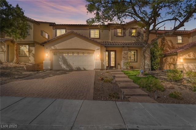 mediterranean / spanish-style house with decorative driveway, a tile roof, an attached garage, and stucco siding