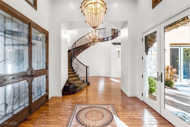 foyer entrance with french doors, an inviting chandelier, light hardwood / wood-style flooring, and a high ceiling