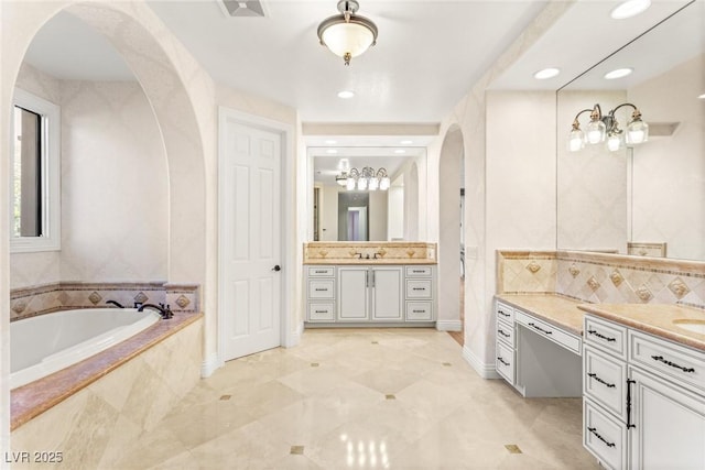 bathroom featuring a relaxing tiled tub, vanity, and decorative backsplash