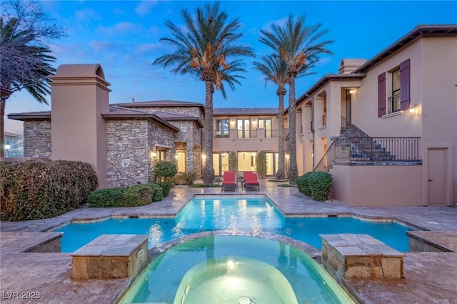 pool at dusk with a patio area and an in ground hot tub