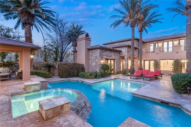 pool at dusk featuring an in ground hot tub and a patio area