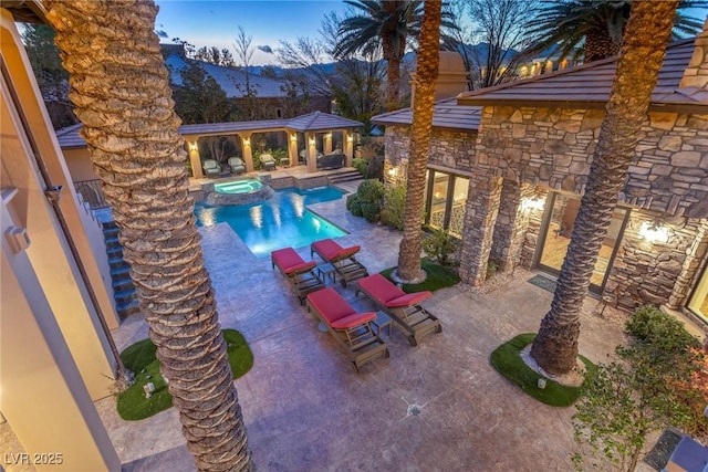 pool at dusk with an in ground hot tub and a patio area