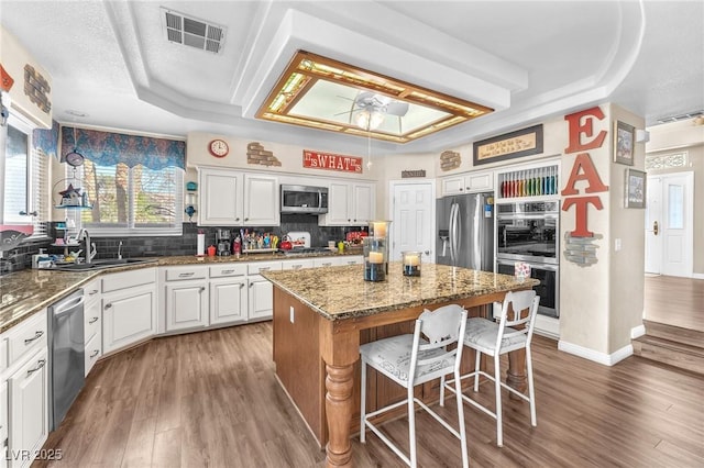 kitchen with dark stone countertops, stainless steel appliances, a tray ceiling, white cabinets, and a kitchen island