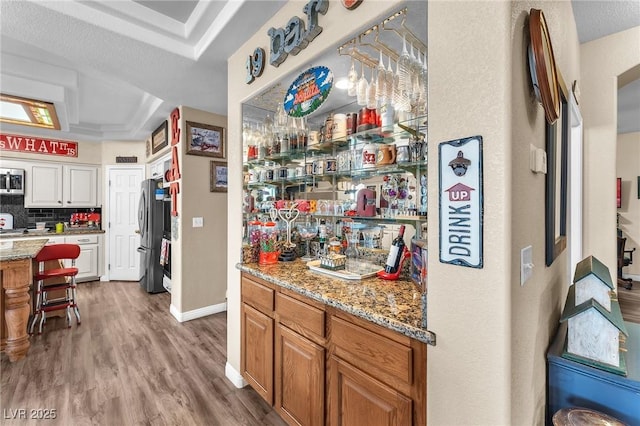 bar with appliances with stainless steel finishes, hardwood / wood-style floors, backsplash, light stone counters, and a raised ceiling