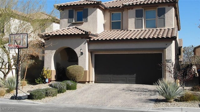 mediterranean / spanish house featuring a garage, a tiled roof, decorative driveway, and stucco siding