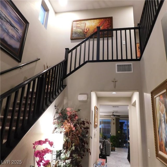 stairway featuring a towering ceiling, visible vents, and a ceiling fan