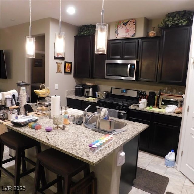 kitchen featuring appliances with stainless steel finishes, a kitchen bar, a center island with sink, and pendant lighting