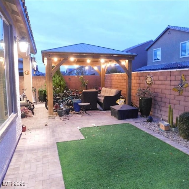 patio terrace at dusk featuring a gazebo, a yard, outdoor lounge area, and a fenced backyard