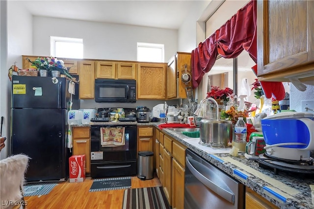 kitchen featuring sink, light hardwood / wood-style flooring, black appliances, and dark stone counters