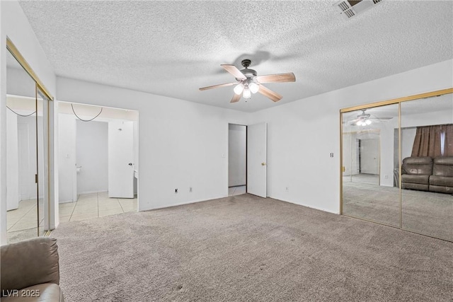 unfurnished bedroom featuring ceiling fan, two closets, light colored carpet, and a textured ceiling