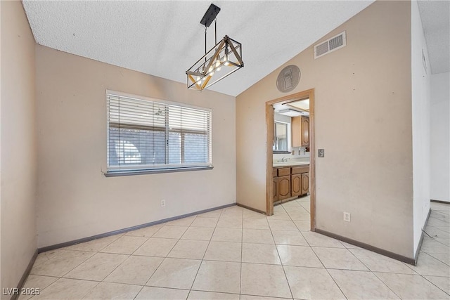 empty room with vaulted ceiling, sink, light tile patterned floors, and a textured ceiling