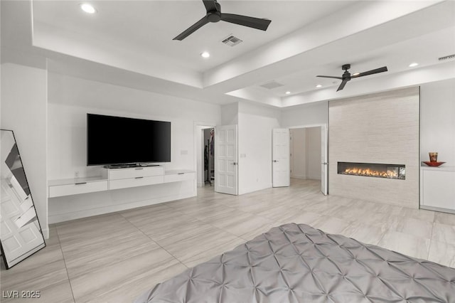 unfurnished living room featuring a tray ceiling, a fireplace, and ceiling fan