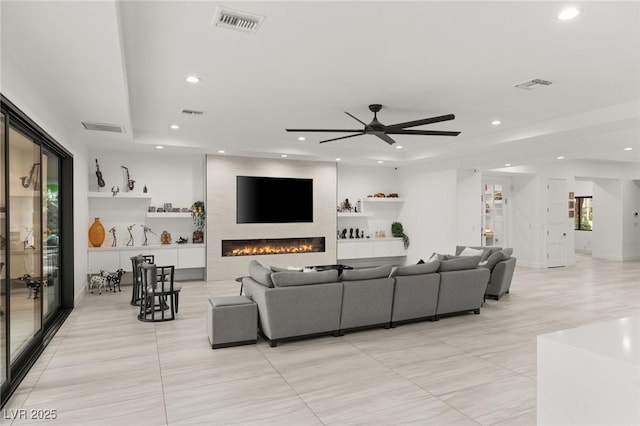 living room with a tray ceiling, a large fireplace, and ceiling fan