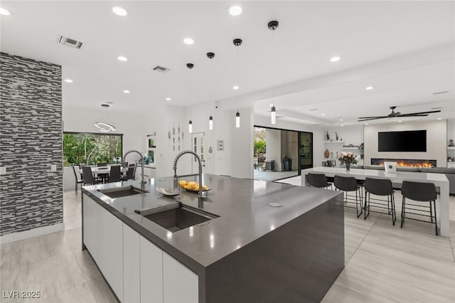 kitchen with a large island, sink, white cabinetry, and pendant lighting