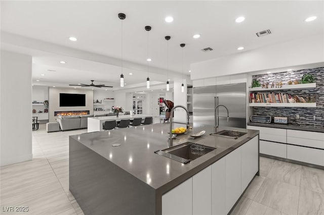 kitchen with sink, built in refrigerator, white cabinetry, a spacious island, and decorative light fixtures