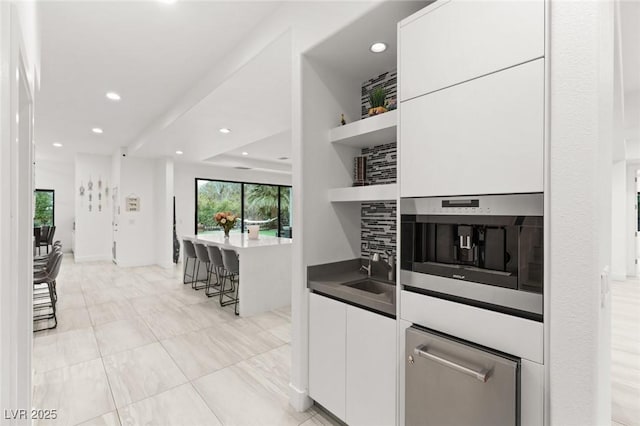 kitchen with white cabinetry, sink, a breakfast bar area, decorative backsplash, and stainless steel oven