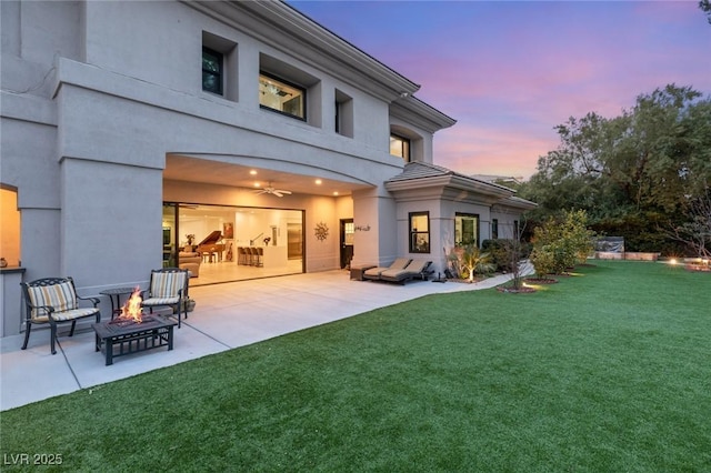 back house at dusk with an outdoor fire pit, a patio area, and a lawn